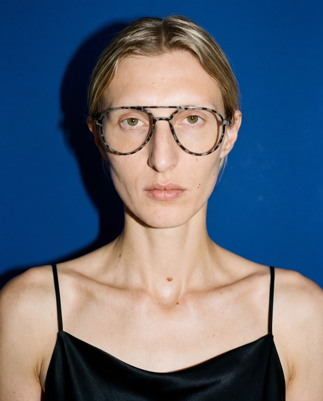 Frau trägt die Einstärkenbrille Lund von Visiloox in Grau-Havana, Editorial-Portrait vor blauem Hintergrund